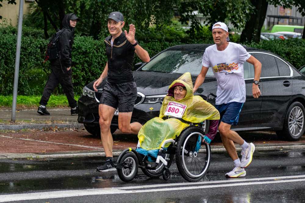 Niezwykła uczestniczka Biegu KoBBiet – pani na wózku inwalidzkim, wspierana przez dwóch mężczyzn na trasie Bieg KoBBiet